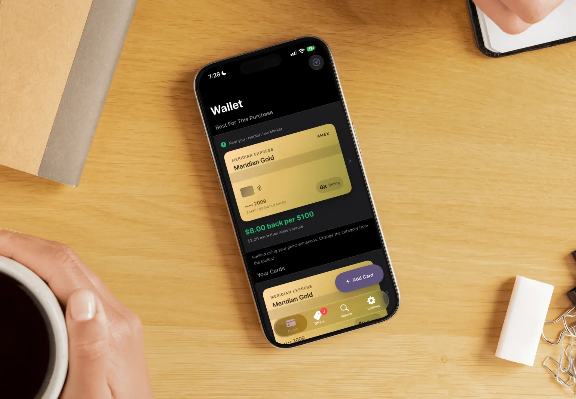 CardSwipe open on an iPhone on a desk beside a cup of coffee, showing the best card for the market nearby